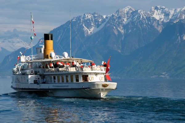 A scenic view of a historic paddle steamer cruising Lake Geneva with the Swiss Alps in the background.